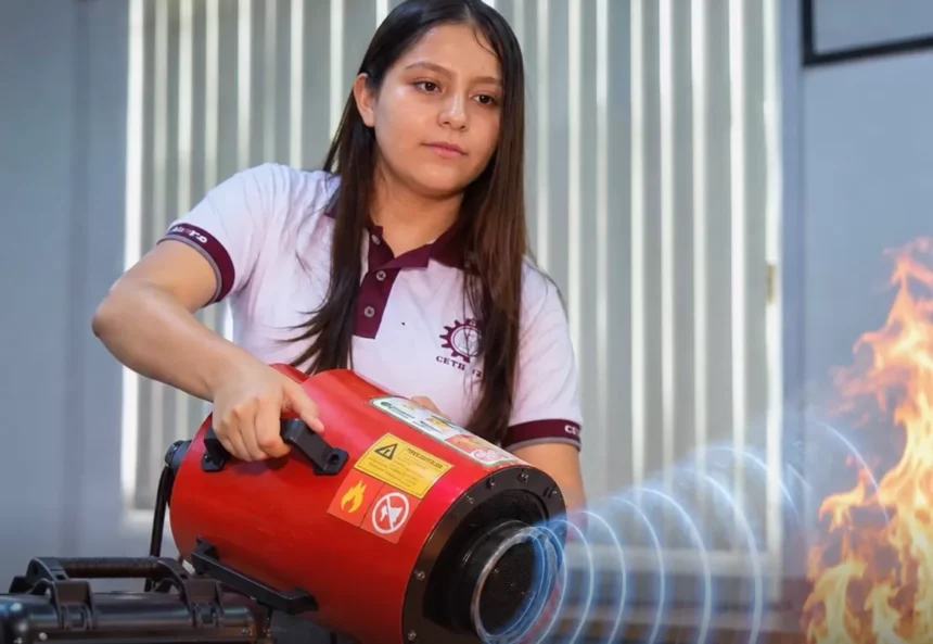 Young woman in a polo shirt operates a red portable fire-safety device aimed at flames during a demonstration.