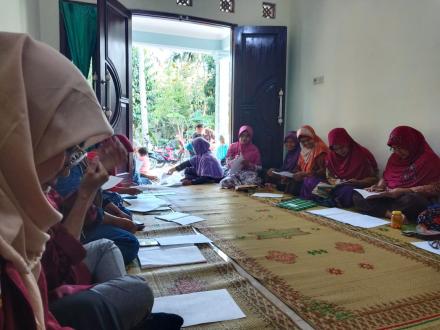 Group of women wearing colorful headscarves sit on a carpeted floor, writing in notebooks during a community class session.