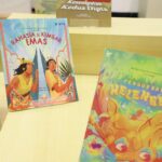 Colorful children's books on a wooden display; left book titled 'Rahasia Si Kembar Emas' shows two kids against a decorative backdrop.