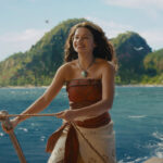 Woman on a boat smiling while holding a rope, with blue sea and a green island in the distance behind her.
