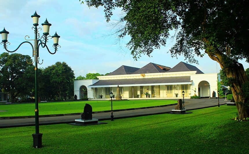 Park scene featuring a white pavilion-like building with arches, black lamp posts, and a green lawn on a sunny day