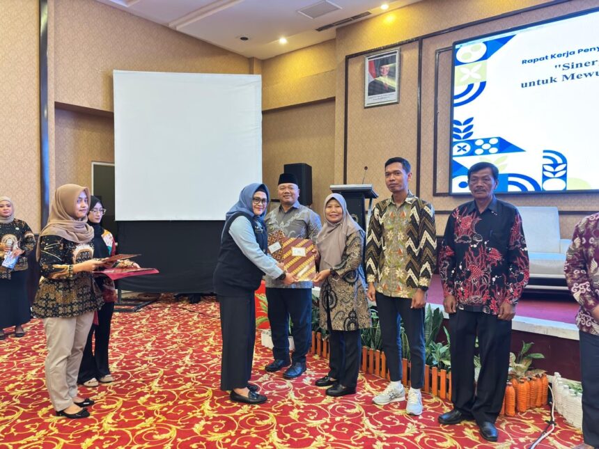 Group of people at an awards ceremony; a woman hands a striped certificate to a man as others look on on a stage with a large screen behind them.