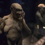 Clay sculpture of a bald, muscular humanoid touching its face, displayed in a glass case.