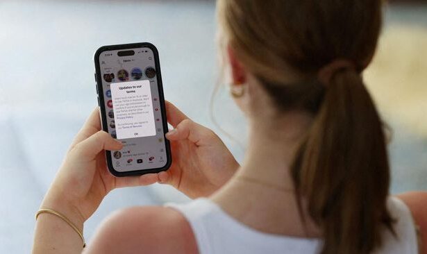 Woman with a ponytail holding a smartphone; the screen shows a messaging notification or chat thread with text visible on the display.