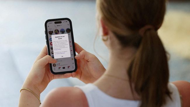 Woman with a ponytail holding a smartphone; the screen shows a messaging notification or chat thread with text visible on the display.