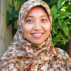 898y71bpqp5ipptdoj06ioq8nnwh - Mabur.co Portrait of a smiling woman wearing a floral hijab, outdoors with green foliage in the background.