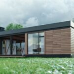 Modern single-story house with wooden cladding and large glass doors, set on a green lawn with a cloudy sky above.