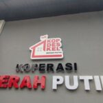 Sign reading KOPERASI MERAH PUTIH with a red roof logo above the text, on a gray wall.