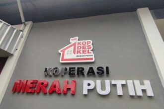 Sign reading KOPERASI MERAH PUTIH with a red roof logo above the text, on a gray wall.