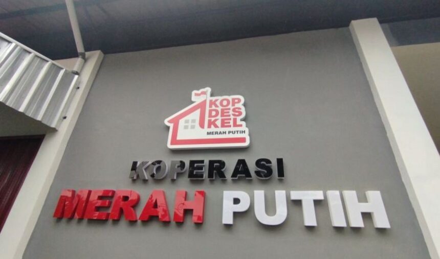 Sign reading KOPERASI MERAH PUTIH with a red roof logo above the text, on a gray wall.