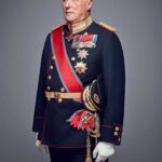 Older man in ceremonial military dress uniform with medals, sash, and sword, standing against a grey backdrop.