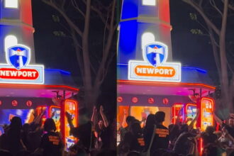 Nighttime scene at a Newport amusement booth with blue and red neon lights and a cheering crowd gathered in front.
