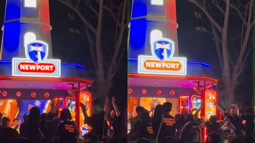 Nighttime scene at a Newport amusement booth with blue and red neon lights and a cheering crowd gathered in front.