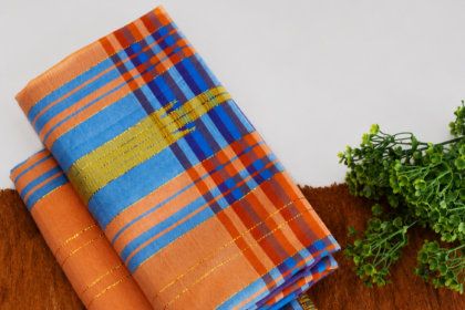 Folded multicolored striped fabric (orange, blue, gold) on a brown surface with a green plant nearby.