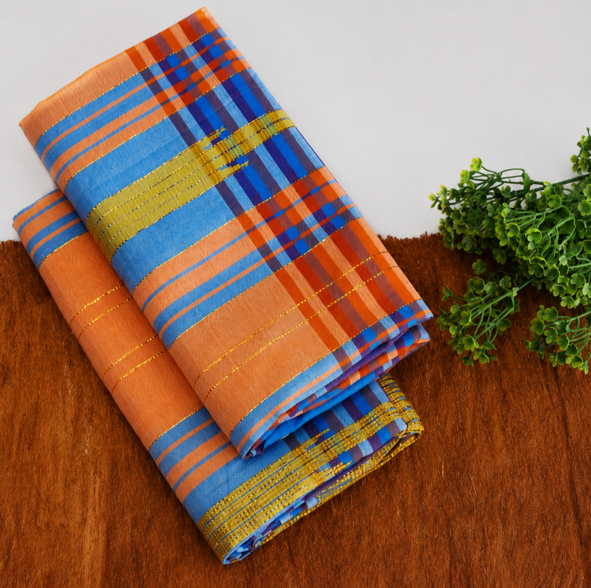 Folded multicolored striped fabric (orange, blue, gold) on a brown surface with a green plant nearby.