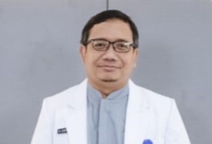 Male doctor wearing a white coat and light blue shirt, with glasses, posing for a portrait against a gray background.