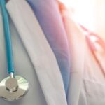 Close-up of a healthcare professional's chest with a blue stethoscope draped around the neck.