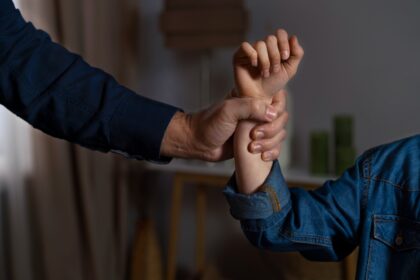 Two people hold each other’s wrists in a firm grip, close-up on their hands against a blurred background.