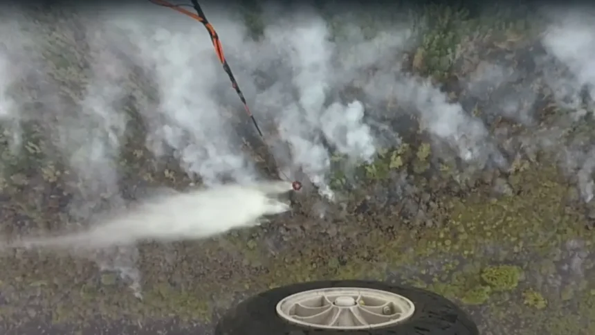 Aerial view of a drone spraying a white mist over a rocky hillside, with a wheel visible in the lower foreground.