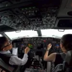 Cockpit view of two pilots in a modern airliner, hands on controls, cockpit panels and screens in front of them during flight.