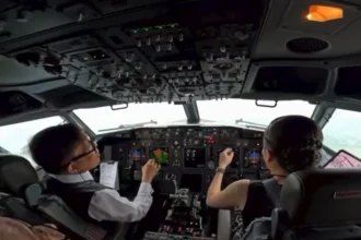 Cockpit view of two pilots in a modern airliner, hands on controls, cockpit panels and screens in front of them during flight.