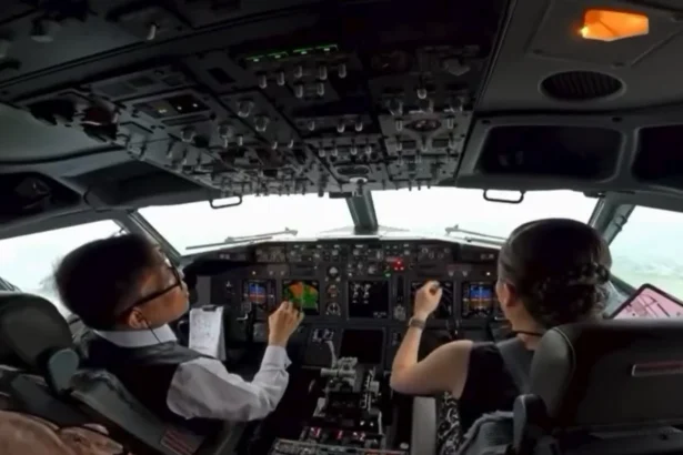 Cockpit view of two pilots in a modern airliner, hands on controls, cockpit panels and screens in front of them during flight.