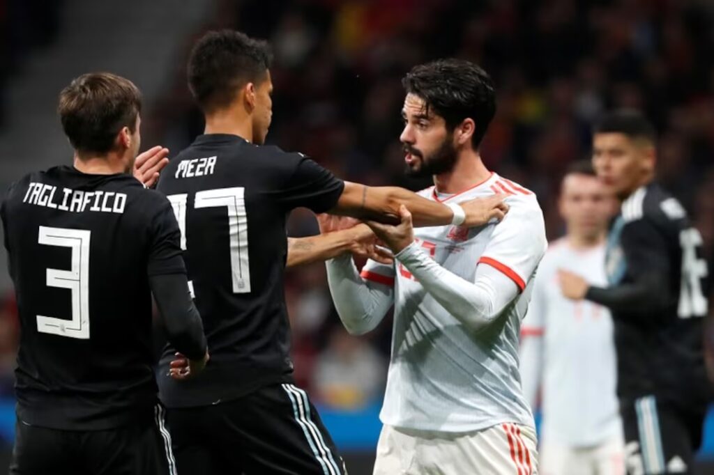 Soccer players collide hands in a tense moment on the field: two players in black jerseys push against a white-jersey opponent during a match.