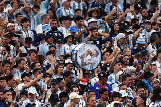 Large cheering crowd in blue-and-white jerseys; a person holds a round drum featuring a kissing couple at center.