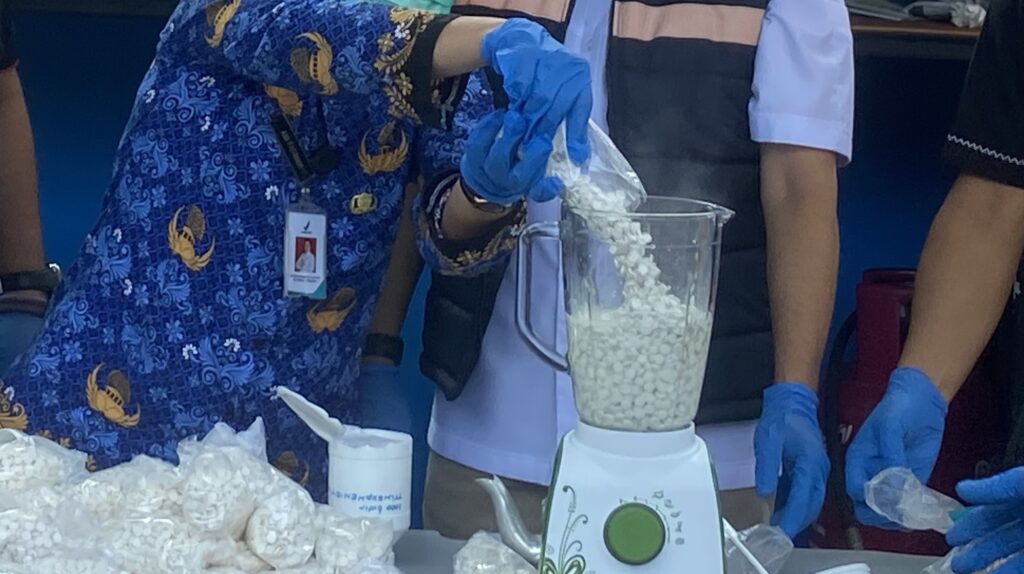 Az - Mabur.co People wearing blue gloves scoop white popcorn into a blender at a market stall.