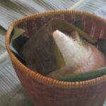 Woven basket with a triangular sticky rice dumpling wrapped in a bamboo leaf.