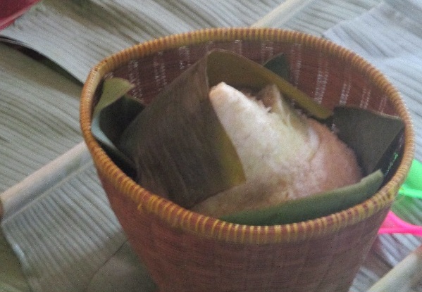 Woven basket with a triangular sticky rice dumpling wrapped in a bamboo leaf.