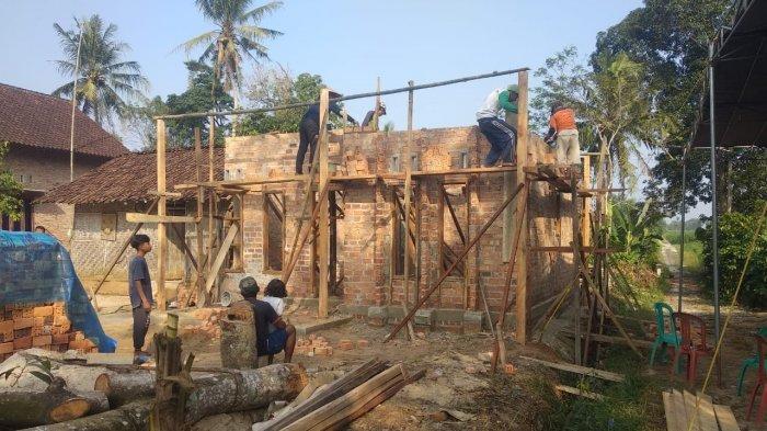 Group of construction workers on wooden scaffolding building a brick wall on a single-story house, outdoors with palm trees in the background
