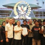 Group of people posing with a signed document in front of a large DPR-RI emblem projection, in a formal indoor setting.