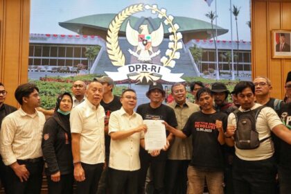 Group of people posing with a signed document in front of a large DPR-RI emblem projection, in a formal indoor setting.
