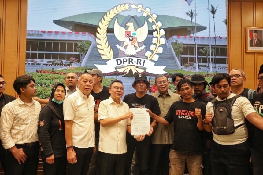 Group of people posing with a signed document in front of a large DPR-RI emblem projection, in a formal indoor setting.