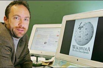 Man sits at a desk with two computer monitors; one displays the Wikimedia globe logo (Wikipedia).