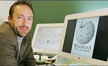 Man sits at a desk with two computer monitors; one displays the Wikimedia globe logo (Wikipedia).