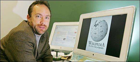 Man sits at a desk with two computer monitors; one displays the Wikimedia globe logo (Wikipedia).