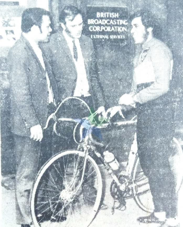 Three men stand around a vintage bicycle with a BBC sign in the background.