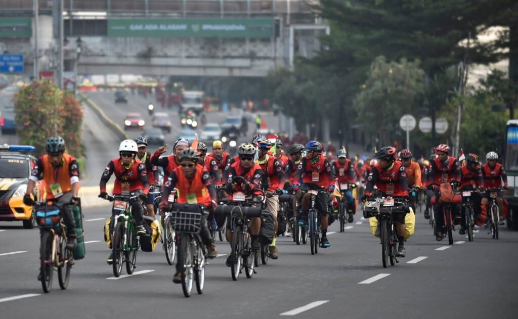 FB_IMG_1783216074587 - Mabur.co Group of cyclists riding on a city street, many in red vests, with support vehicles nearby during a march or ride event.