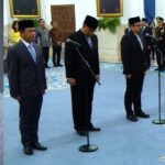 Portrait of a man with glasses and a goatee on the left; the right side shows a formal ceremony with suited men wearing songkoks standing at microphone stands in a grand room.