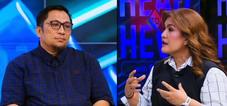 Two TV hosts on a talk-show set; man with glasses in a blue plaid shirt on the left and a woman in a white checkered blouse with a black vest on the right, gesturing as they talk.