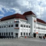 White multi-story bank building with red-tiled roof and BNI signs along a curved street.
