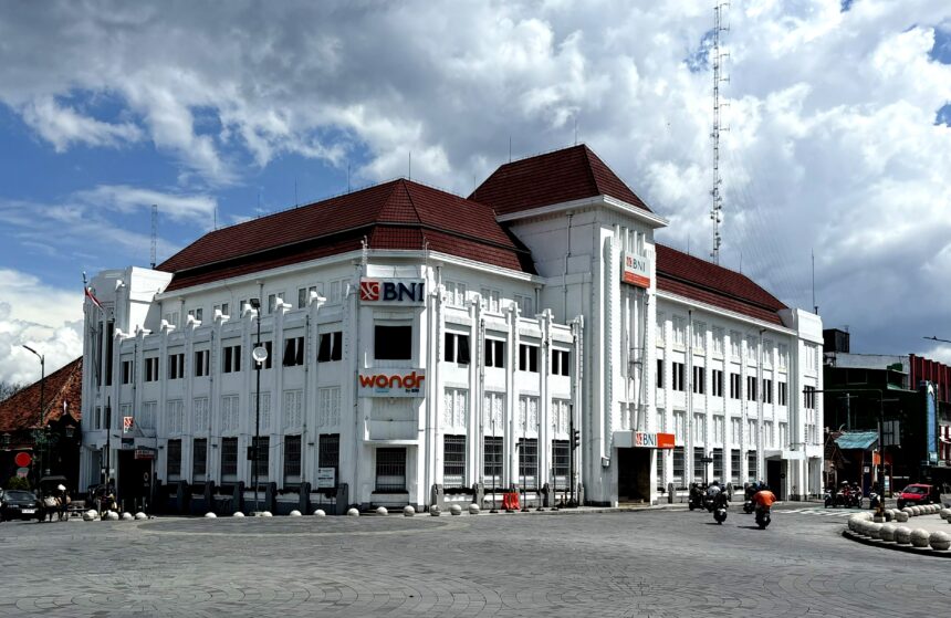 White multi-story bank building with red-tiled roof and BNI signs along a curved street.