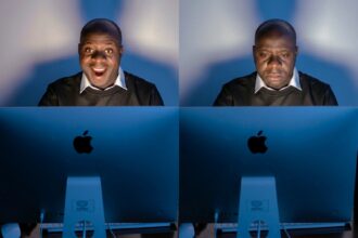 Two men sit side by side at blue Apple computer monitors; left man smiles broadly, right man looks down in a somber mood.