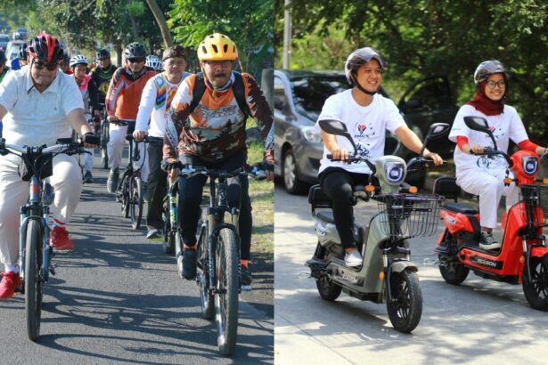 A large group of cyclists wearing helmets ride together on a sunny street; front riders in casual shirts and colorful jerseys.