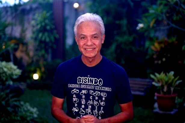 Smiling older man with white hair, wearing a Bisindo T-shirt, standing in a garden at dusk.