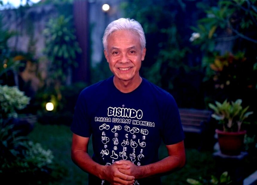 Smiling older man with white hair, wearing a Bisindo T-shirt, standing in a garden at dusk.