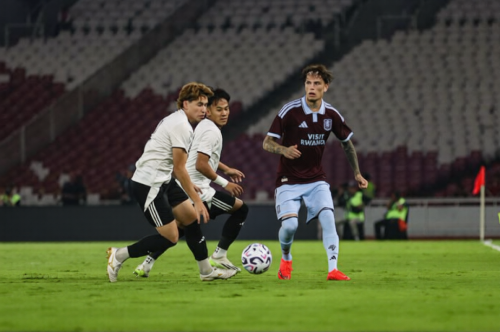 Garnacho GBK by bolasport-ezremove - Mabur.co Soccer player in maroon jersey dribbles a ball while two opponents in white chase him on a green field in a stadium.