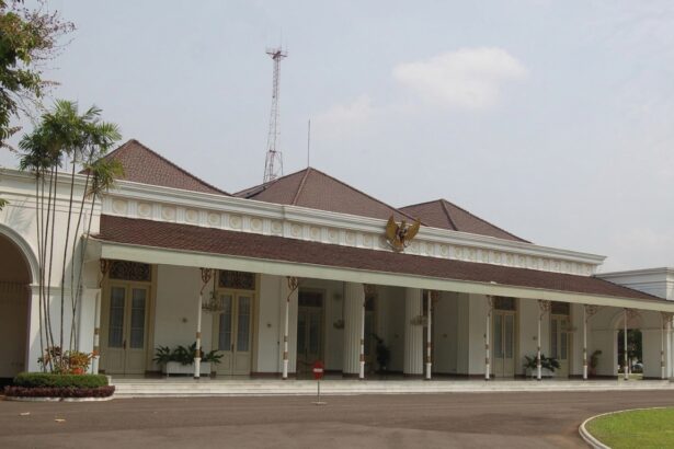 White colonial-style public building with a red-tiled roof, arched entrance, and a row of columns along a covered veranda; palm trees to the left.